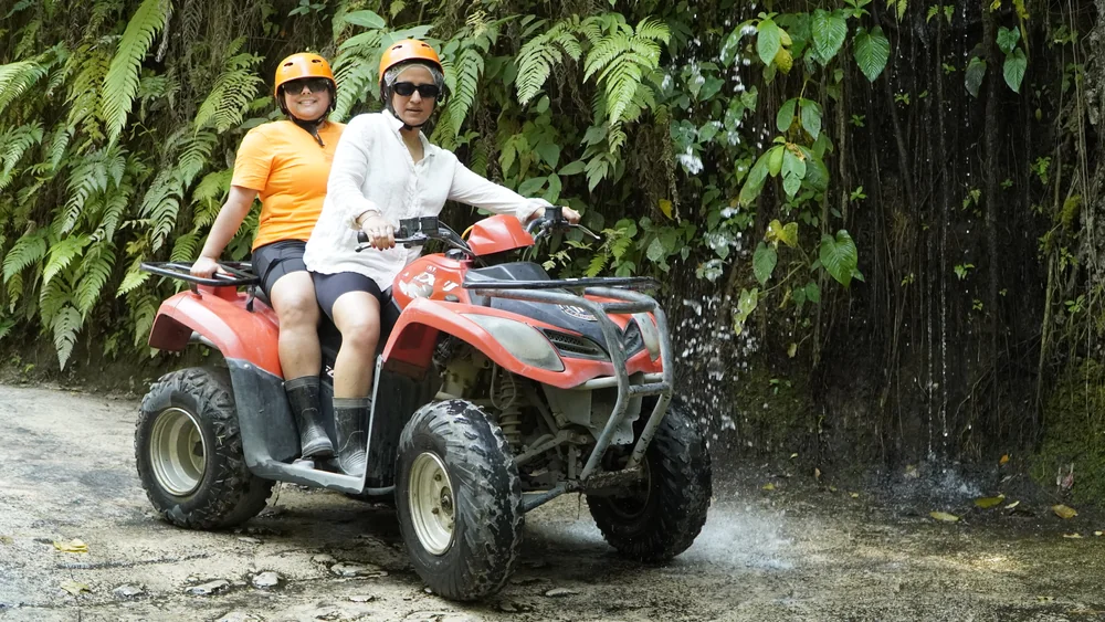 Tandem riders posing with ATV in front of a natural hanging green vine wall