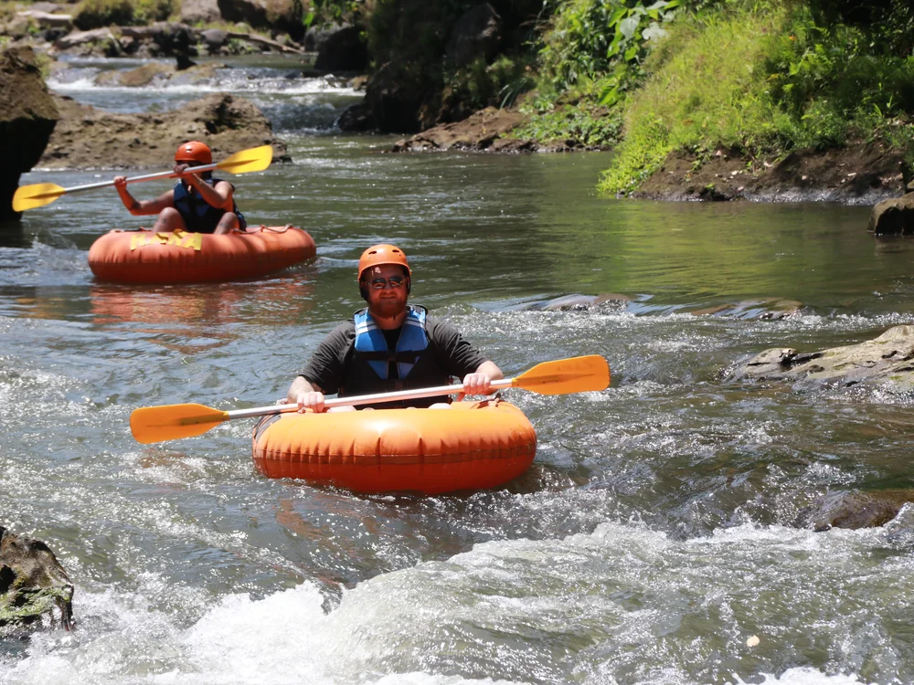 Two river tubers gliding peacefully through lush green rock canyon
